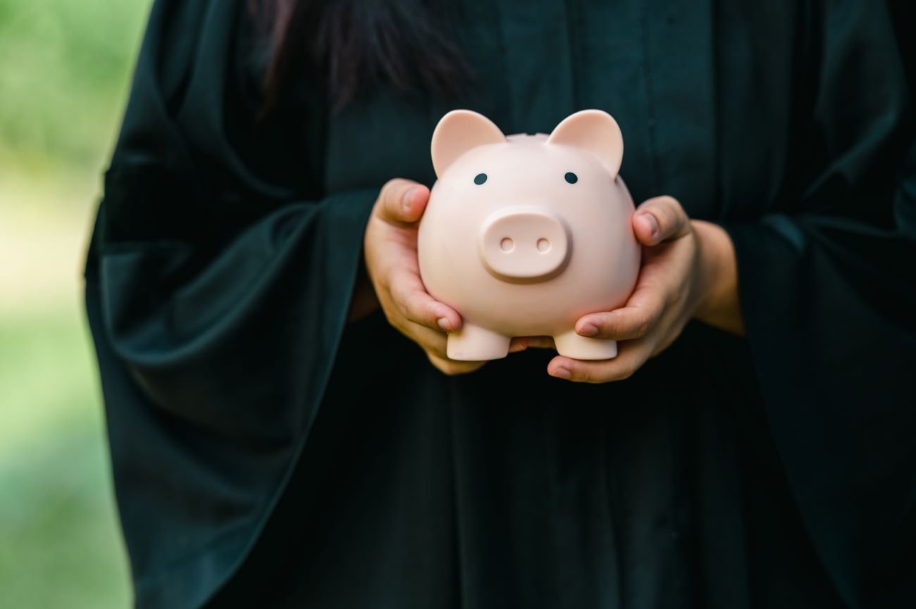 graduate in robe holding a piggy bank