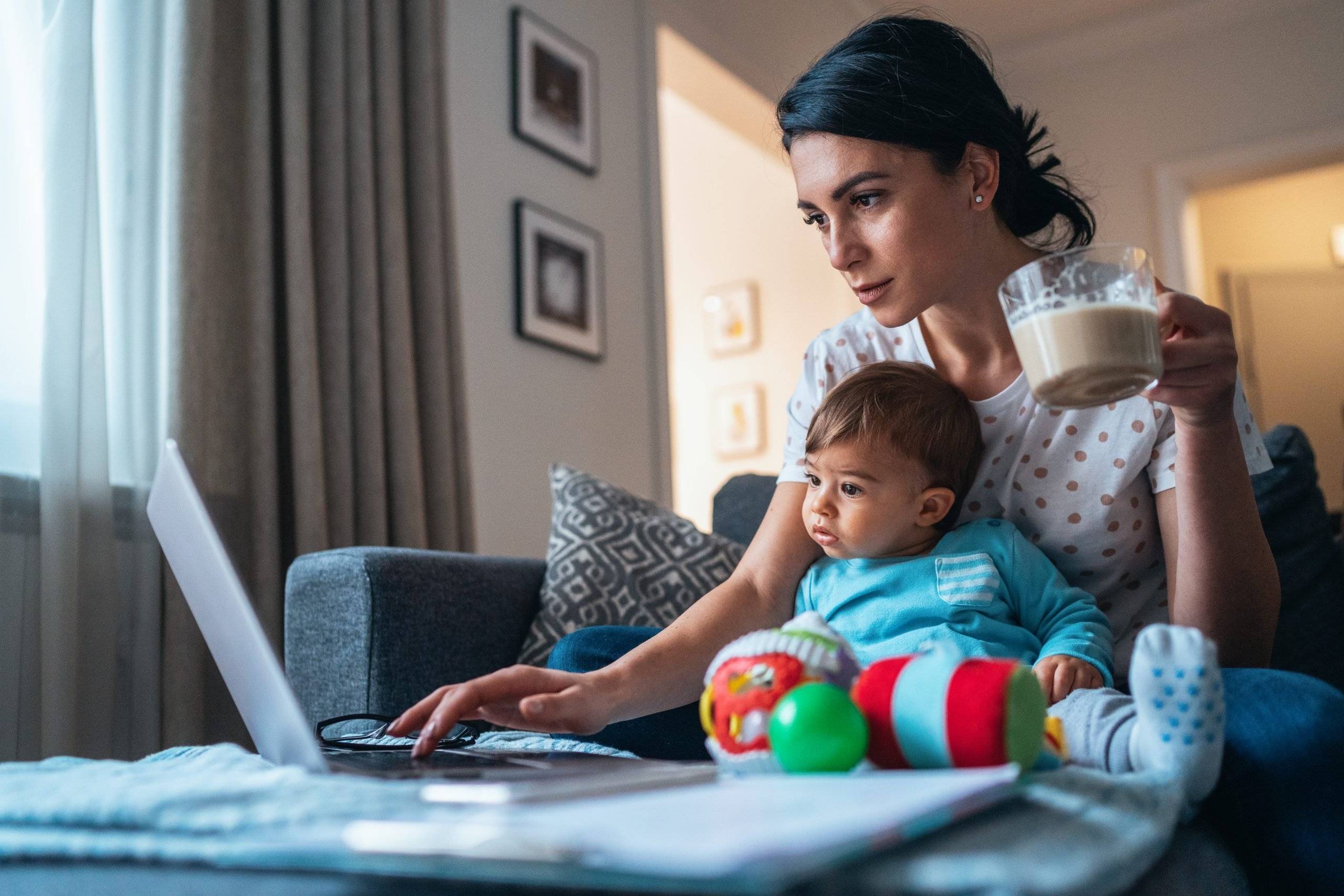 Young modern mother with a baby using laptop at home. Looking to attend college as a parent.