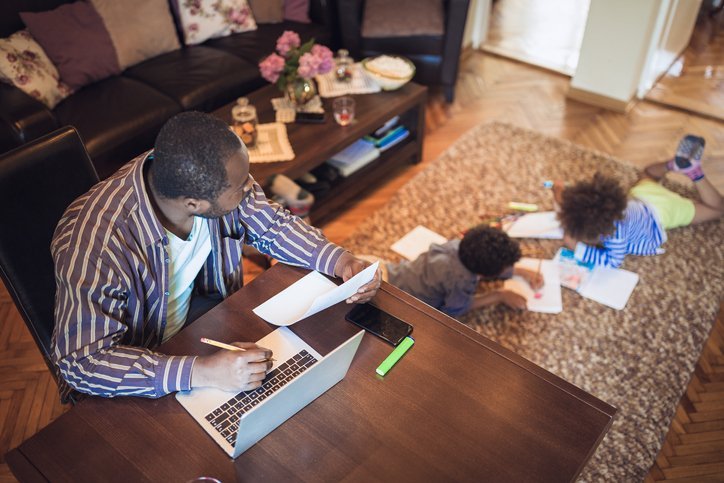 A middle-aged dad watches his kids as he works on a laptop